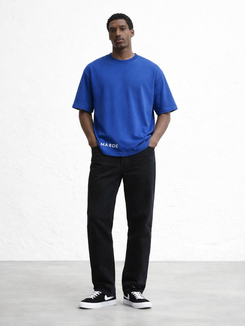 Man wearing a blue t-shirt and black pants standing against a white background
