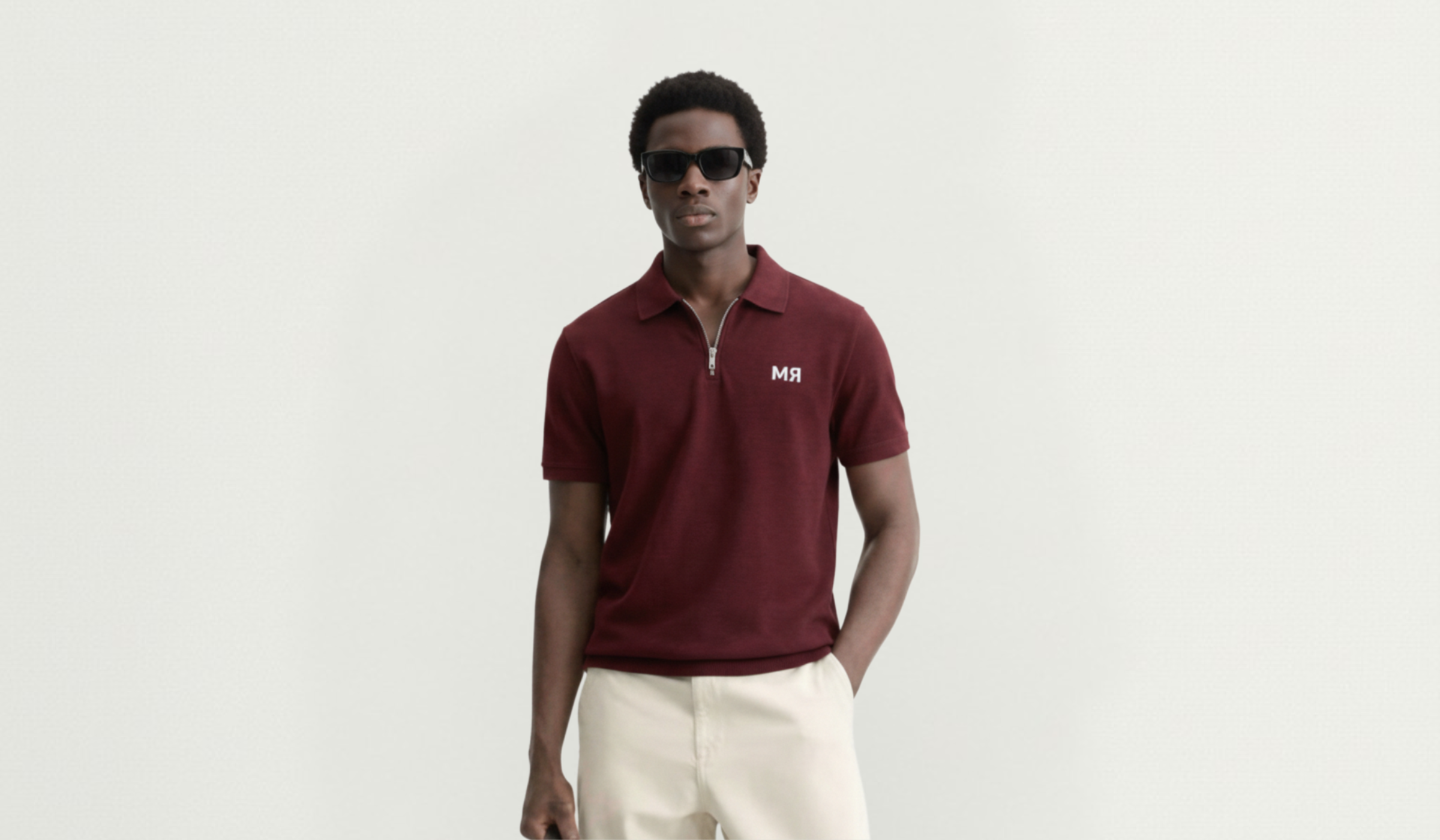 Man wearing a burgundy polo shirt with a logo on a light gray background